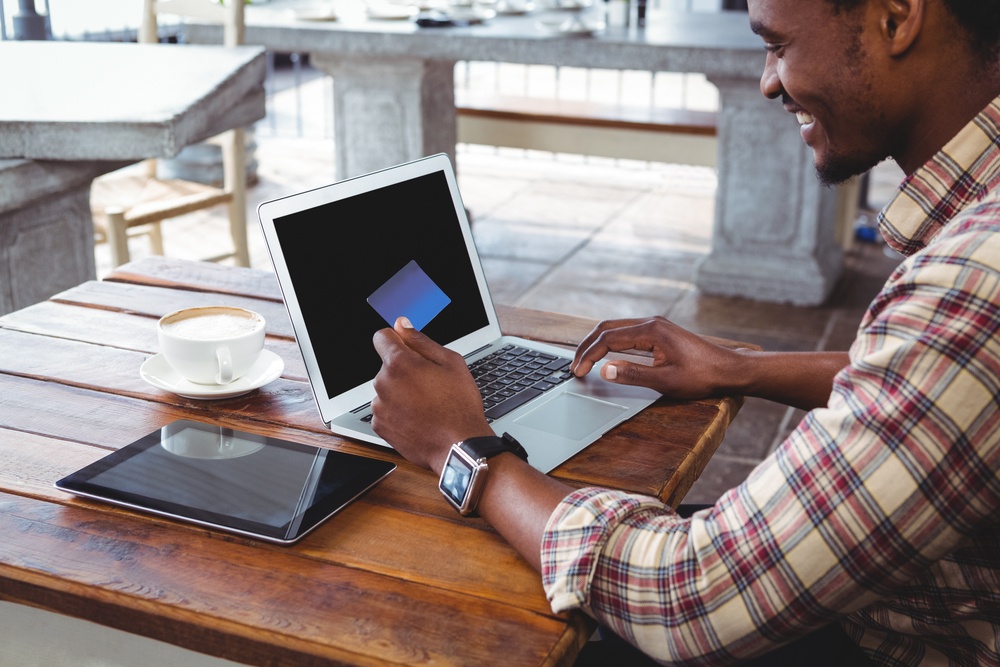 Man doing online shopping with credit card on laptop in cafeteria